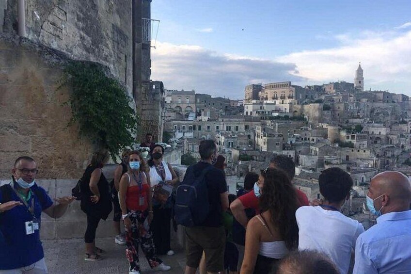 A group of people standing on a ledge overlooking a historic cityscape with layered buildings and a prominent tower. 5