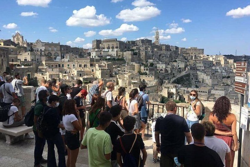 A group of tourists observing a historic cityscape with layered buildings and a prominent tower. 4