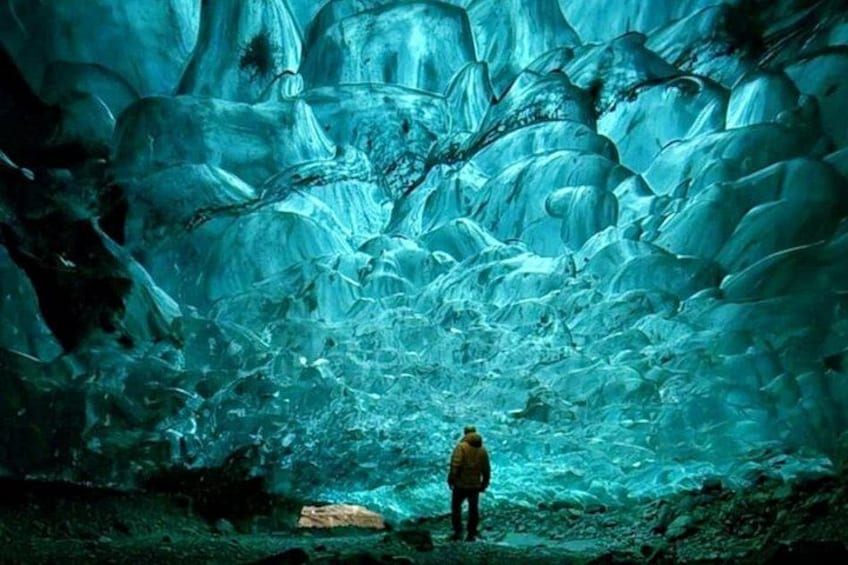 A person standing in a cave with blue ice formations. 1