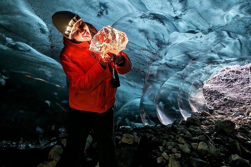 Una persona con una chaqueta roja sosteniendo un bloque de hielo grande en una cueva glaciar. 4