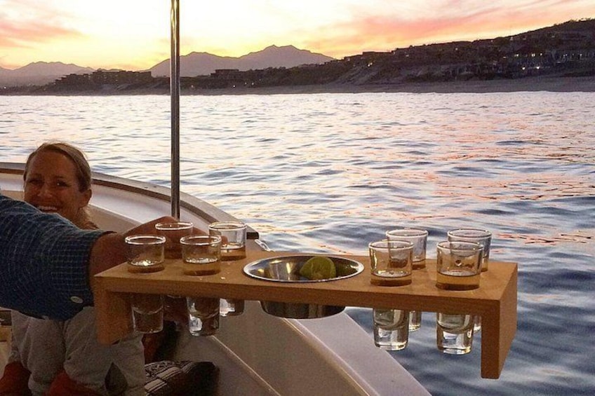 A boat with a wooden table holding glasses and a bowl, set against a sunset over water. 3