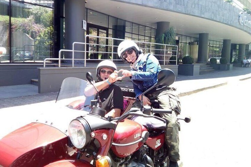 Two people on a red motorcycle in front of a building. 4