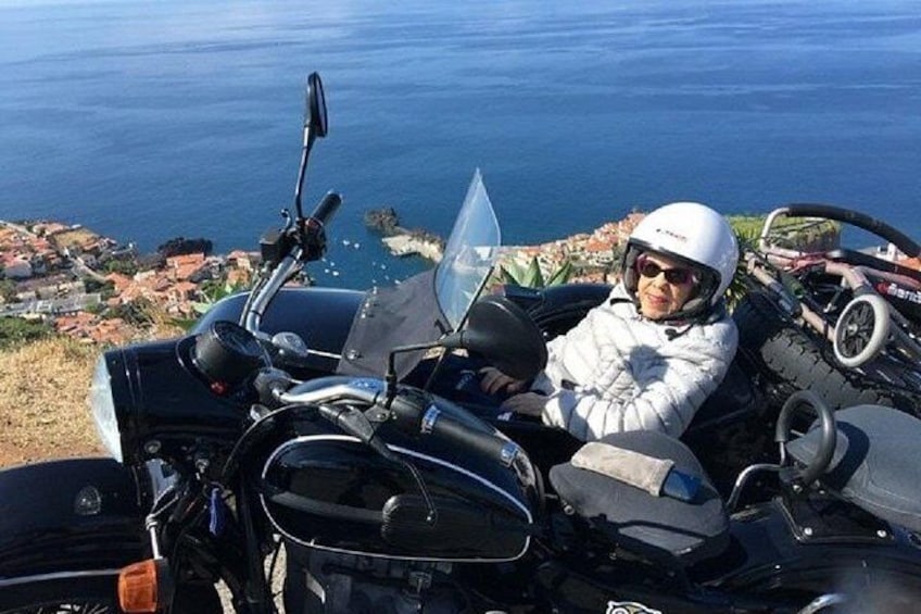 A person sitting on a motorcycle with a helmet, overlooking a coastal landscape. 3