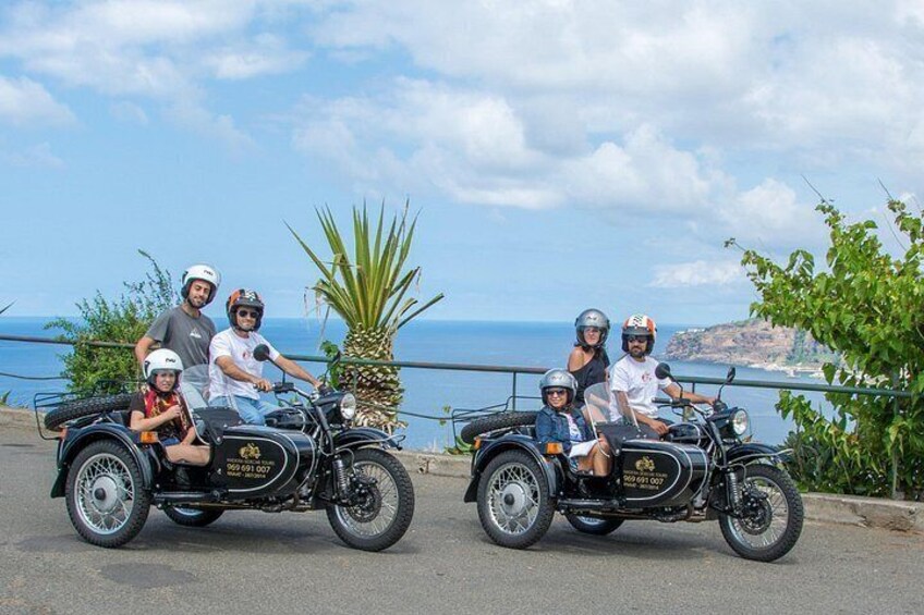 A group of people on a motorcycle tour, with a scenic coastal background. 1