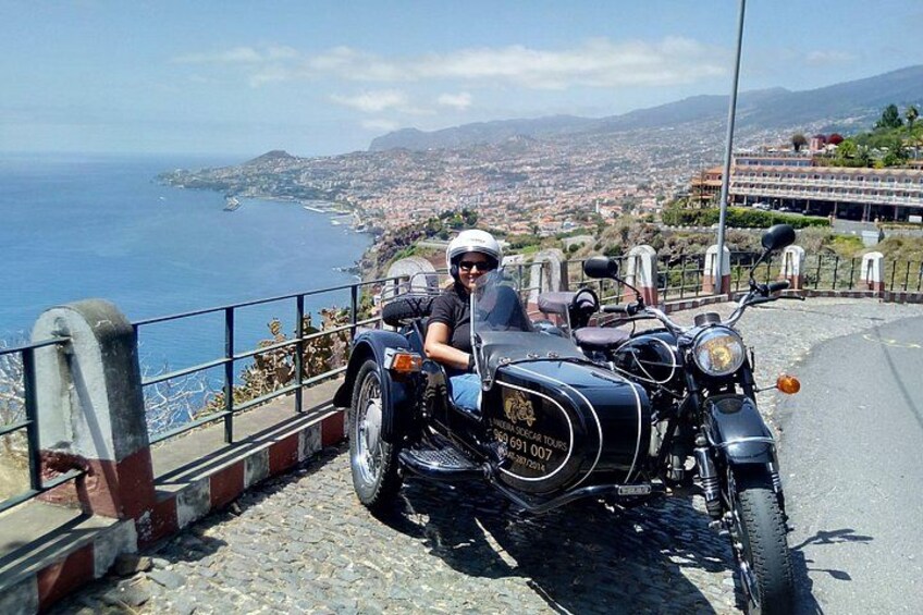 A motorcycle parked on a cobblestone road with a coastal cityscape in the background. 2