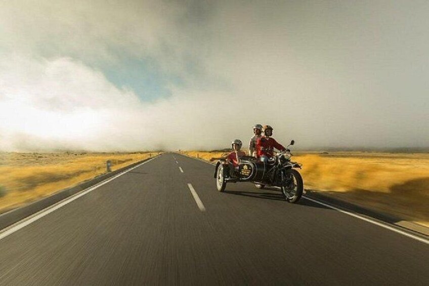 A motorcycle with a sidecar on a road in a desert landscape. 2
