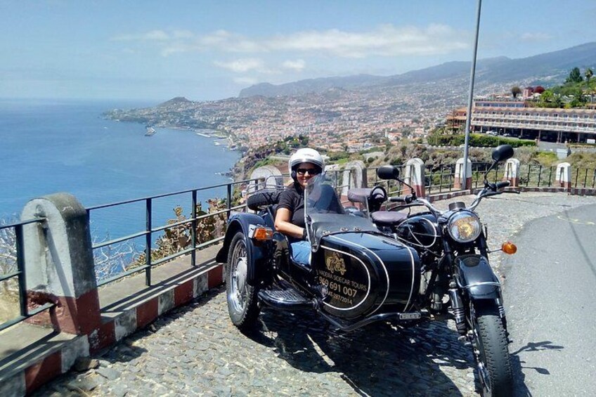 A motorcycle parked on a cobblestone path with a coastal view in the background. 2