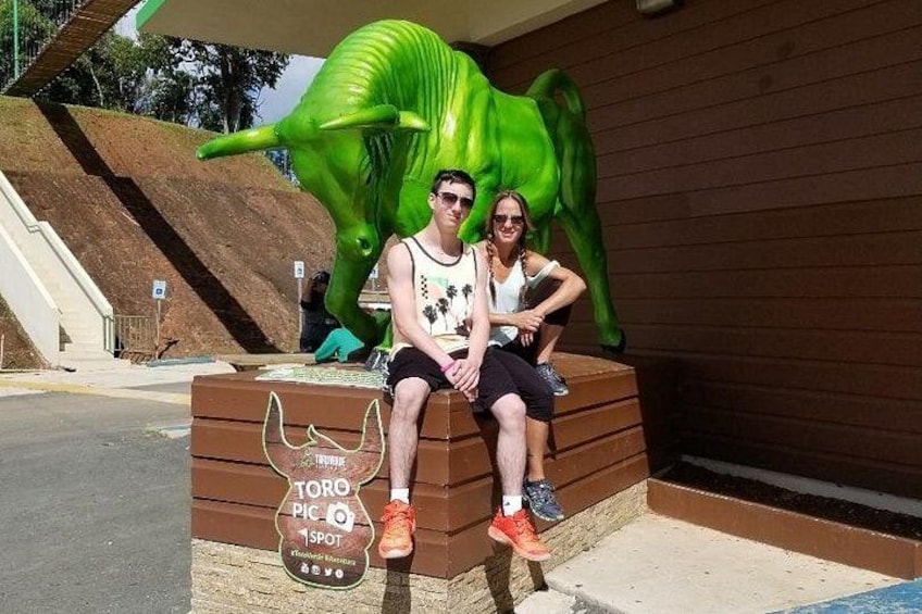 Two people sitting on a bench with a large green dinosaur sculpture behind them. 2