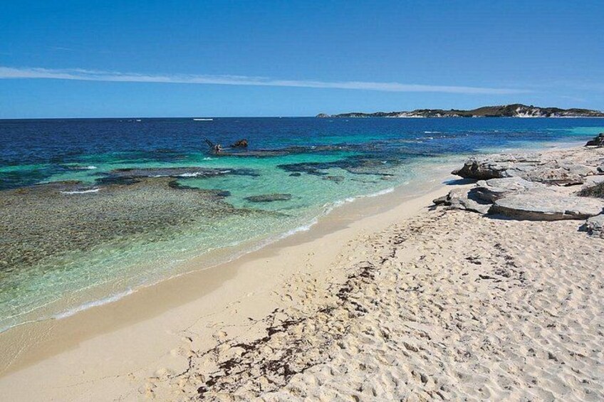 En strand med kristallklart turkosfärgat vatten, en sandstrand och klippiga utskjutande partier. 4