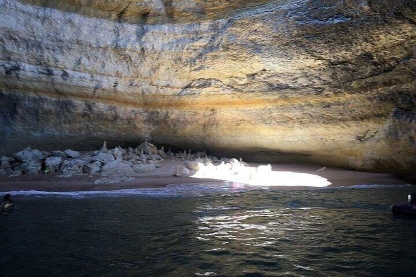 Una cueva con un cuerpo de agua en su interior, una orilla rocosa y luz solar filtrándose. 4