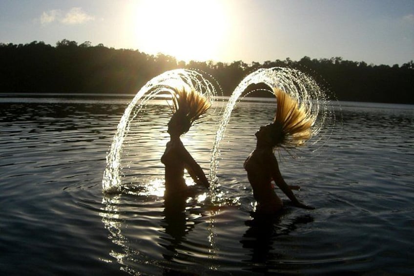 Two people performing water tricks in a lake with the sun setting in the background. 4