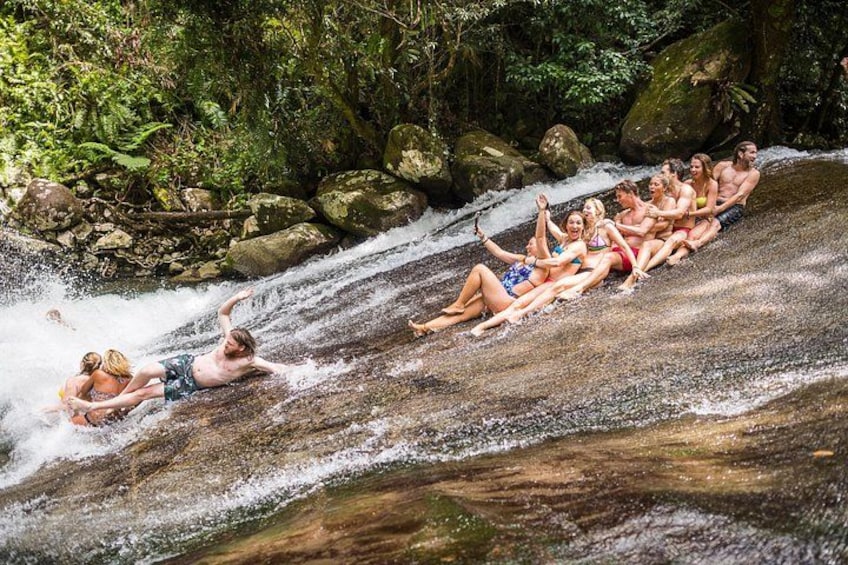 A group of people sliding down a water slide in a forested area. 1