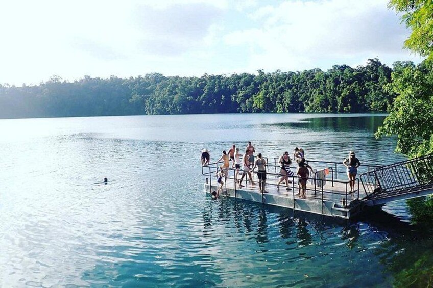 A group of people on a dock extending into a lake surrounded by trees. 2