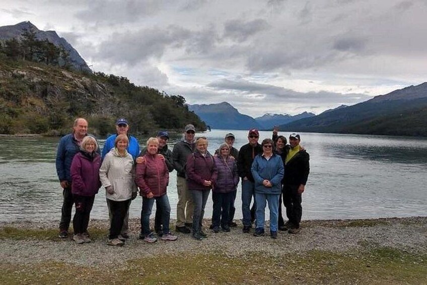 Een groep mensen staat bij een meer, met bergen op de achtergrond. 3