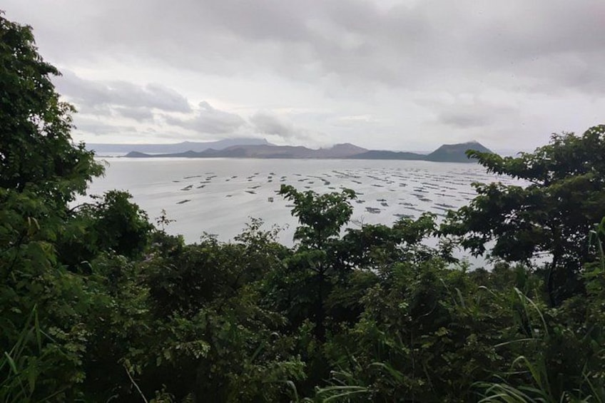 A body of water with boats, surrounded by dense foliage and distant mountains under a cloudy sky. 5