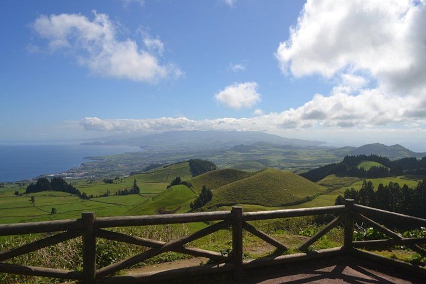 Vista panorámica de colinas onduladas, una valla de madera y una costa lejana bajo un cielo parcialmente nublado. 2