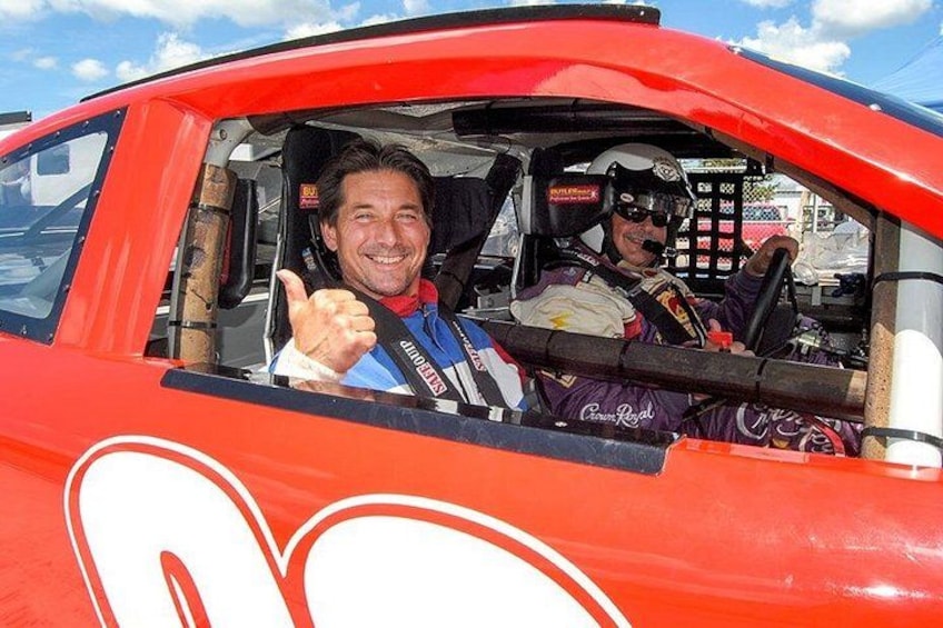 Een persoon in een raceauto die een duimpje omhoog steekt. 3