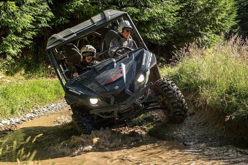 A four-wheeled off-road vehicle navigating a muddy trail in a forested area. 2