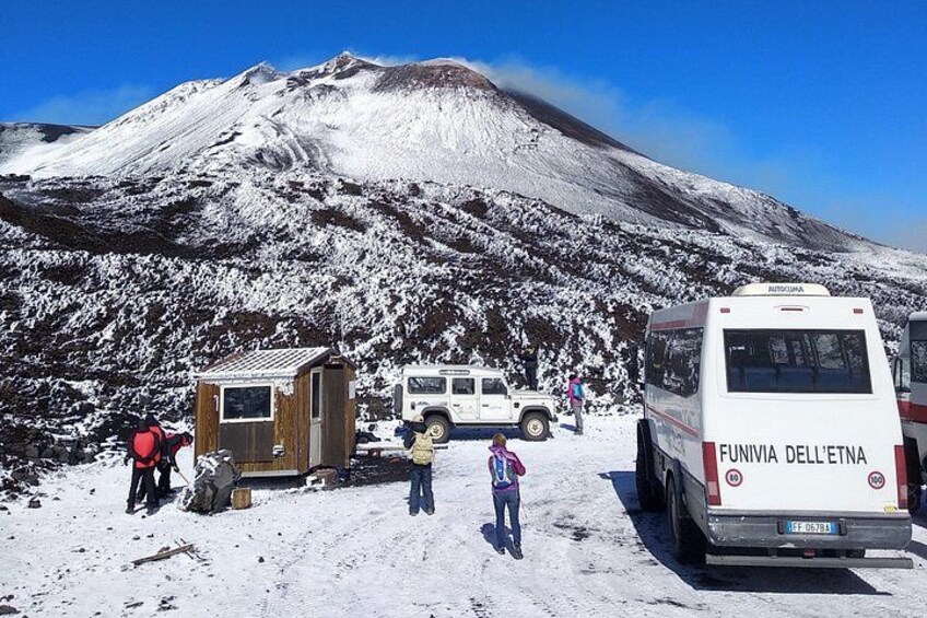 A snow-covered mountain, a small wooden shelter, a white bus, and a few people. 2