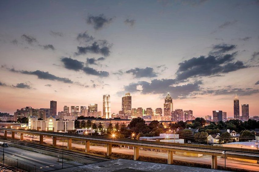 A city skyline at dusk with illuminated buildings and a highway in the foreground. 1