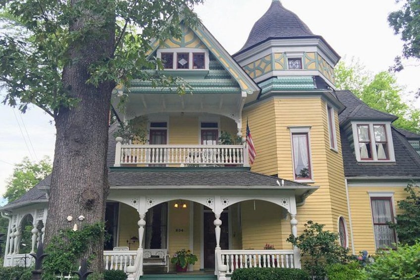 A yellow Victorian-style house with a wrap-around porch, a turret, and a large tree in front. 5