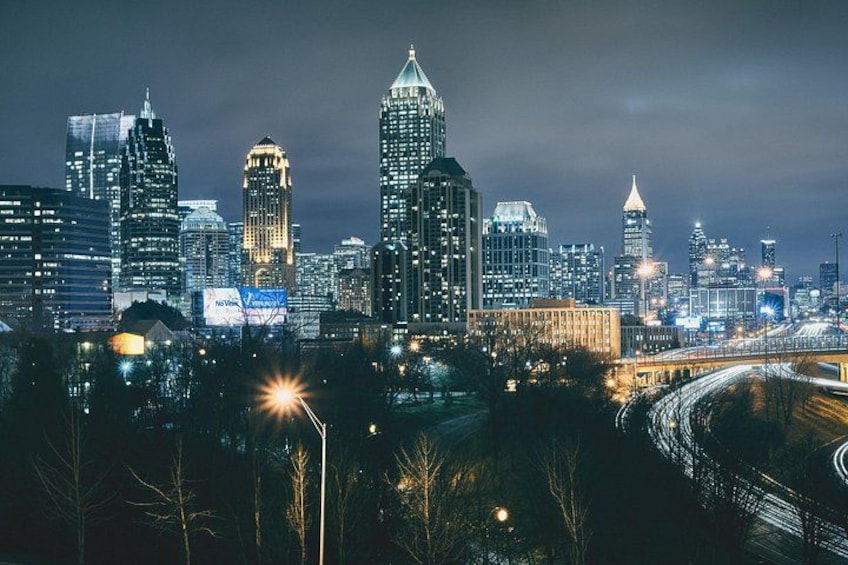 A city skyline at night with illuminated buildings and a highway. 2