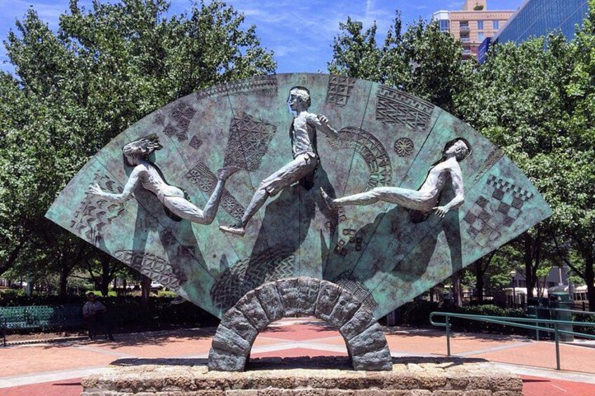 A bronze sculpture of three figures in a park with trees and a building in the background. 4