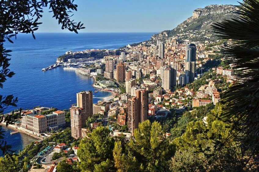 Un paysage urbain côtier avec des bâtiments imposants, une mer bleue et limpide, et une chaîne de montagnes en arrière-plan. 2