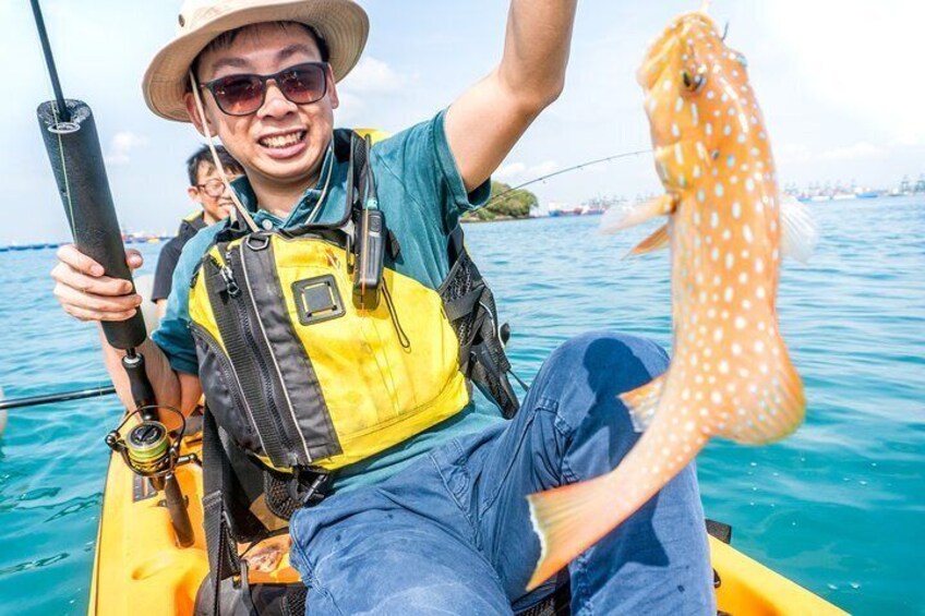 Eine Person in einem gelben Boot hält eine Angel und einen Fisch. 1