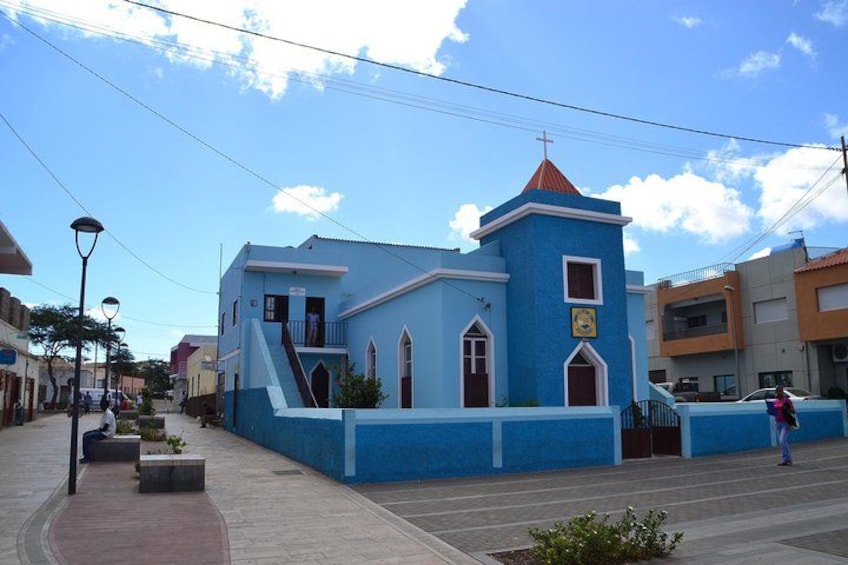 Una iglesia azul con techo rojo, una cruz y un campanario. 3