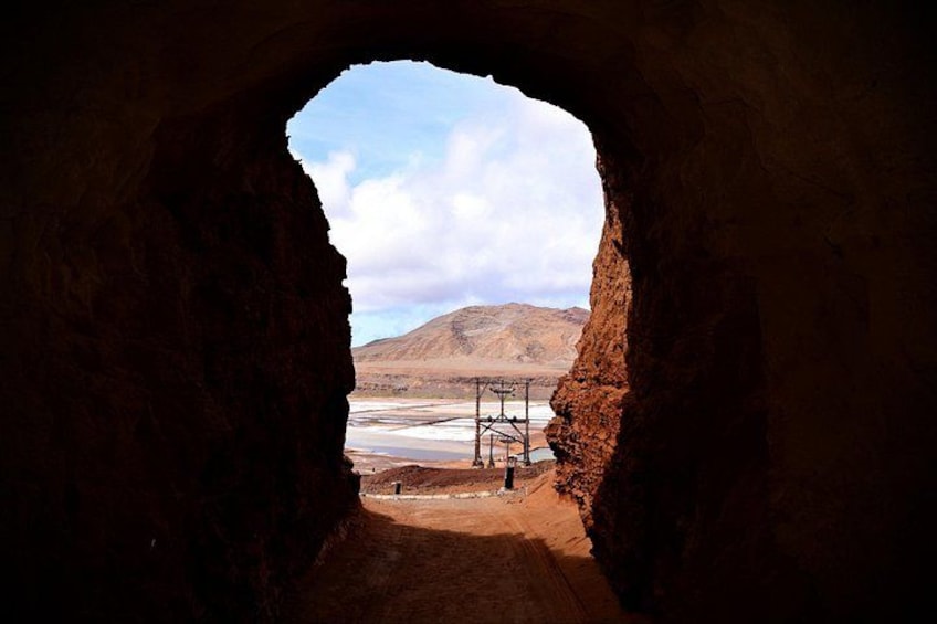 A cave opening with a view of a dry landscape and a metal structure in the distance. 4