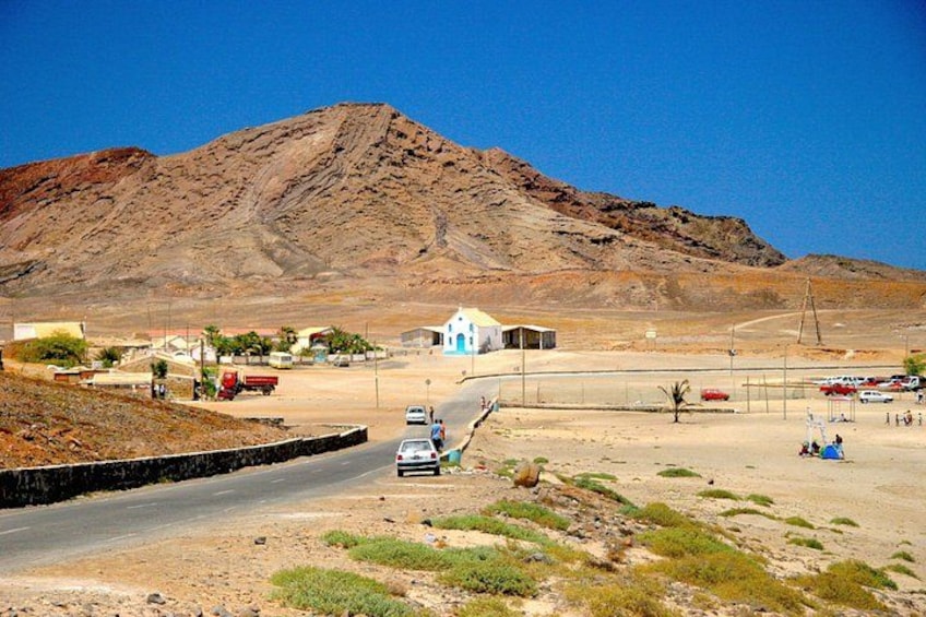 A desert landscape with a mountain, a road, a few vehicles, and sparse vegetation. 5