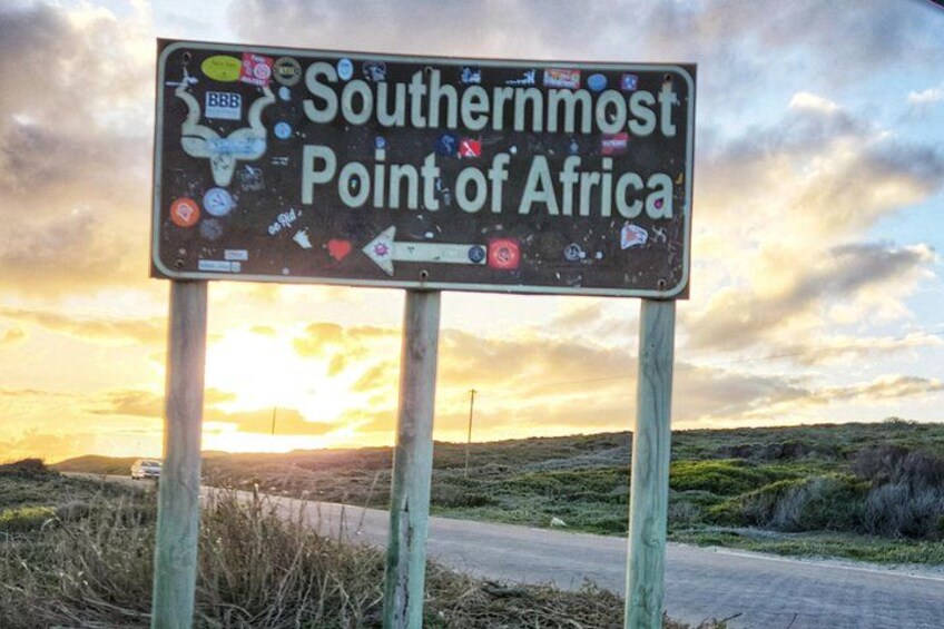 A signpost with stickers, titled 'Southernmost Point of Africa,' with a sunset in the background. 4