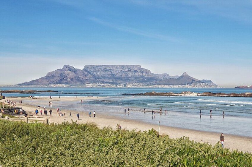 A beach with people, a mountain, and a ship in the distance. 2