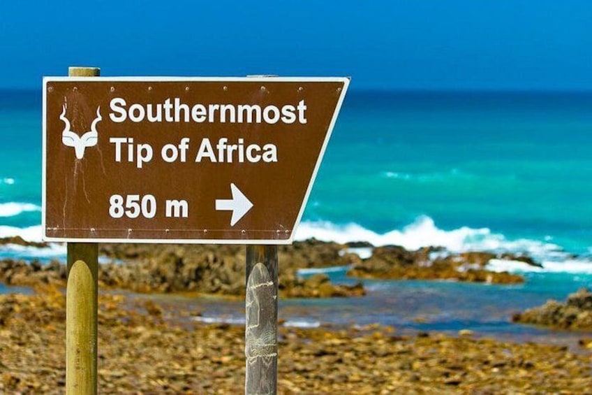 A sign indicating the Southernmost Tip of Africa at 850 meters, with a view of the ocean and rocky shore. 1