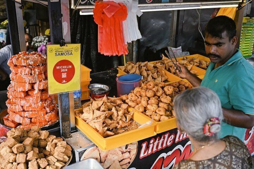 A street food vendor stall with various fried snacks and a sign for 'Michelin 2024'. 2