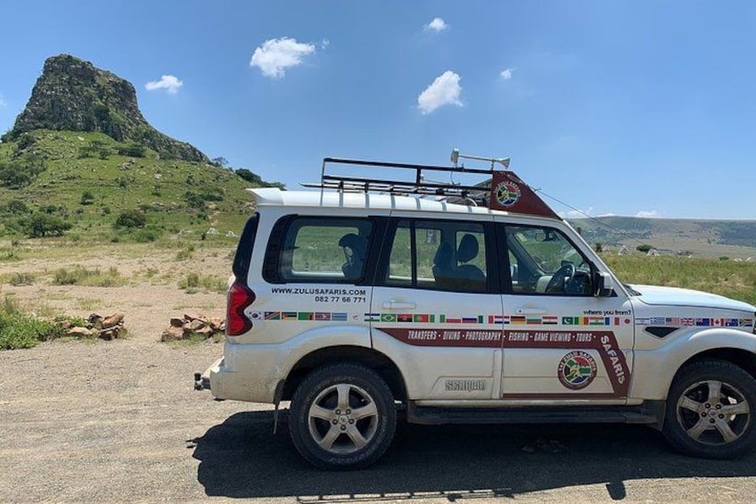 A safari vehicle parked on a road with a rocky hill in the background. 3