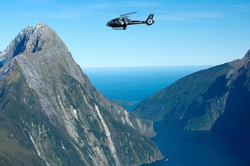 En helikopter flyver over et bjergrigt landskab med frit udsyn til havet nedenfor. 1