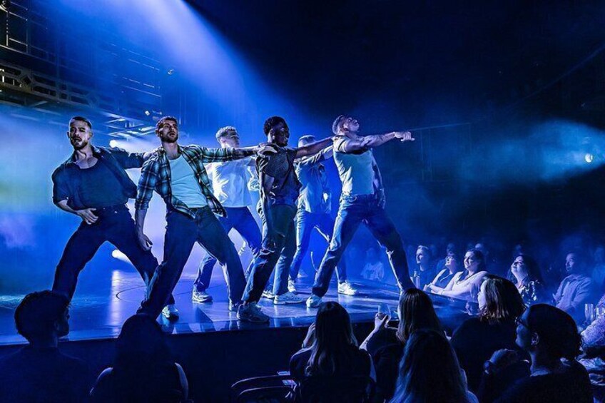 En grupp dansare uppträder på scenen inför en publik i en lokal med dämpad belysning. 5
