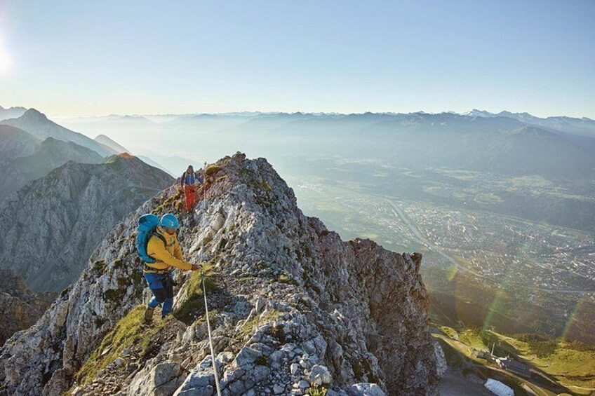 Ein Wanderer auf einem felsigen Berggipfel mit einer Stadtlandschaft im Hintergrund. 1