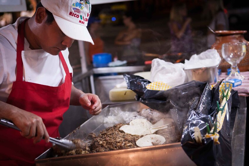 A person cooking in a large pot, wearing a red apron and a cap with text. 3