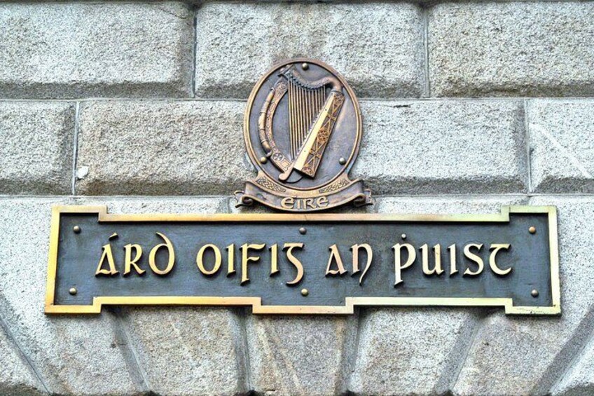 Un letrero con el emblema de un arpa y el texto 'ÁRd Oifis an Púist' sobre una pared de piedra. 5