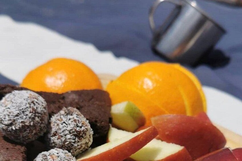 A plate with food items including a brownie, orange, apple slices, and a cup. 5