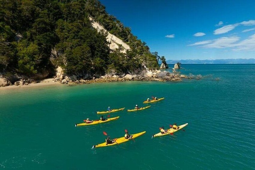 A group of kayaks on calm turquoise waters, surrounded by a coastal landscape with dense green foliage and rocky outcrops. 3