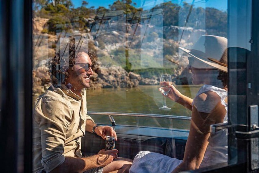 Deux personnes se trouvent sur un bateau, l’une tenant un verre d’eau, avec une côte rocheuse en arrière-plan. 5