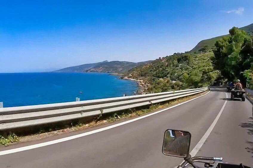A coastal road with a guardrail, a motorcyclist, and a clear blue sea. 5