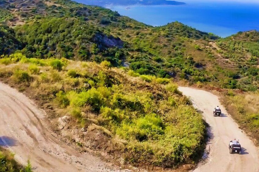 A winding dirt road with vehicles, surrounded by green hills and a coastal view. 3