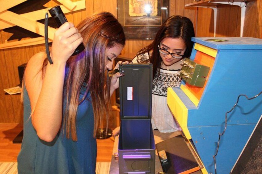 Two individuals examining a blue and yellow electronic device, possibly a computer or a gaming console, in a room with wooden walls and a framed picture. 3