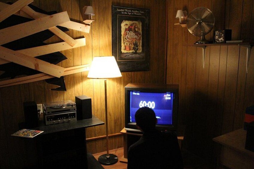 A room with wooden walls, a lamp, a television displaying a timer, and a fan. 1
