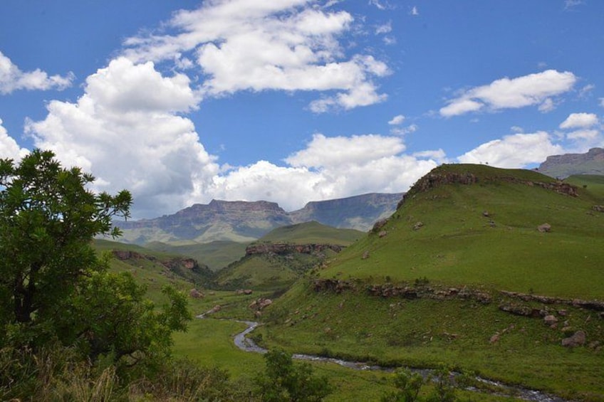 A valley with a river, green hills, and distant mountains under a partly cloudy sky. 3